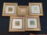 Photo of five miniature framed prints arranged on a dark cloth, showcasing their gold-toned frames and colorful landscapes.