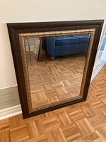 Full view of the decorative wood framed square mirror with dark and gold frame showing parquet floor reflection.
