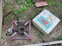 Photo showing the propane burner unit along with its original cardboard packaging box placed on gravel ground outdoors.