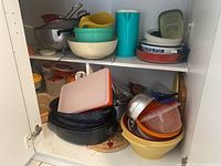 Shelf with various kitchen items: enamel roasting pans, plastic food storage containers, cutting boards, colanders, mixing bowls