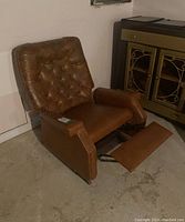 Brown vinyl reclining rocking chair angled showing side, backrest buttons tufted upholstery and wooden armrest accents, footrest extended.