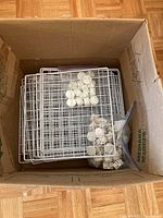 Photo showing metal wire shelving panels stacked inside a cardboard box, along with plastic connectors in sealed bags.