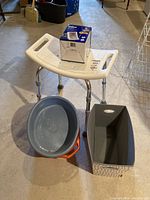 White plastic shower chair with drainage holes, metal legs, blood pressure monitor box on top, two plastic pails below.