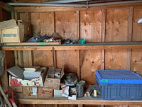 Wide view of wooden shelf with cardboard boxes containing ceramic tiles, metal hardware, brackets, and blue plastic bins.