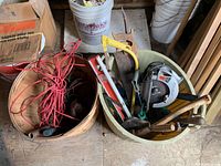 Photo showing assorted hand tools including hammers, hand saws, a lever, an axe, and a coiled red extension cord in two baskets.
