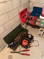 Three metal toolboxes on basement floor filled with assorted hand tools and power tools, shown from side angle