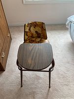 Front view showing floral upholstery backrest and attached wooden table surface on metal frame chair.