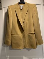 Front view of mustard yellow silk jacket with one button and two front pockets on hanger