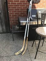 Two Koho Ultimate 2100 senior hockey sticks leaning against a brick wall outside, showing full length including blades and shafts