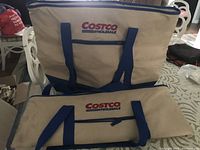 Two large Costco insulated bags, one fully expanded and one folded, beige with blue handles and Costco Wholesale logo