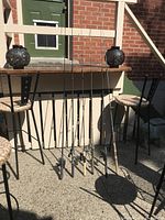 Full view of five fishing poles leaning against a wall outdoors on concrete ground, showing overall condition and setup.