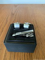 Front view of cufflinks and tie clip set displayed in black box on wooden surface.