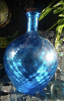 Photo of blue glass round bottle showing embossed pattern and glossy surface reflecting light.