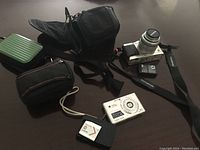 Overview of two cameras, multiple camera cases, Sony battery, and charger cable displayed on a dark surface.