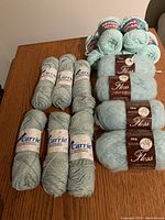 Overall shot showing the grouping of 15 yarn skeins on a wooden table, including Bernat, Carrie, and Floss brands.