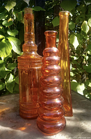 Three distinct orange glass bottles outdoors with leaves in background, showing full lot.