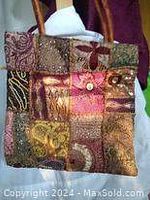 Full front view of a hand stitched patchwork bag with various fabric patches, beads, and sequins in copper and brown tones, with two medium brown handles.