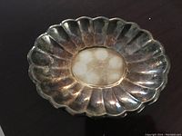 Photo of an old fluted silver plate with tarnish and patina on a dark surface.
