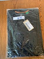 Black men's long sleeve shirt in original sealed packaging laying on wooden floor.