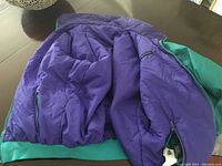 Columbia reversible ski jacket in purple and green, opened to show inside lining and zipper with tags.