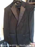 Front view of black men's tuxedo jacket with satin peaked lapels on a hanger.
