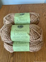 Top-down image showing 3 balls of organic cotton yarn with green labels, stacked on wood table