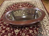 View from above showing the oval glass inset top with wood border against a patterned carpet background.