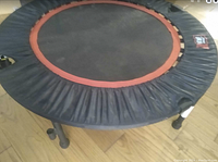 Photo showing the full round personal trampoline with black jumping surface, orange border, and black edge cover along with sturdy legs.