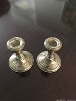 Pair of short round-base silver candlesticks with classical design and visible patina.