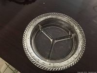Top view of a round sterling silver dish with a decorative thick rim and a clear glass insert divided into three triangular sections for holding olives or condiments.