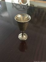 Photo of a single sterling silver goblet on a dark reflective table surface showing its overall shape and condition.