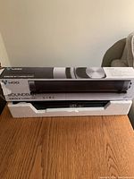 WOO soundbar in original packaging with the box and styrofoam insert for protection, showing front and side views of the box and soundbar.