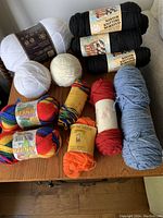 All yarn skeins and balls displayed on a wooden surface, showing various colors and brands