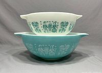 Side view of two Pyrex mixing bowls stacked, one turquoise with white Amish Butterprint design and one white with turquoise design