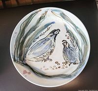Front view of pottery plate showing hand-painted design of two quails surrounded by leaves and seeds in natural colors.