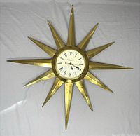 Full front view of the gold-tone starburst metal electric wall clock by Ingraham on a light sheet background.