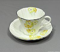 Teacup and saucer set with yellow flowers and black trim on white porcelain, viewed from the front and side
