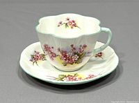 Front view of Shelley teacup placed on saucer, showing pink blossom floral design and scalloped edges.