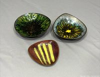 Top-down view of three vintage Mid-Century Modern enameled trinket dishes showing designs and colors.