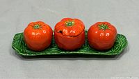 Front view of the full set showing three tomato-shaped containers on a green leaf tray.