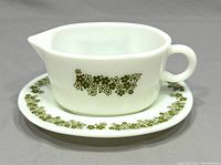Front and side angle view of the white glass gravy boat with green floral Crazy Daisy pattern and attached saucer.
