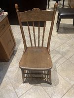 Solid wood chair from the front showing carved floral design on the backrest, spindle supports, contoured seat, and turned legs.