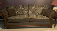 Full front view of brown sofa couch with floral cushioned upholstery and wooden frame, along with two dark brown throw pillows on arms.