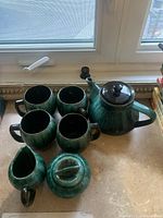 Green glass tea set arranged on countertop near window, showing all pieces including teapot, cups, creamer, and sugar bowl.