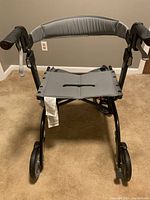 Front view of a gray Drive Nitro 4-wheel rollator walker, showing padded seat and hand brakes on the handles.