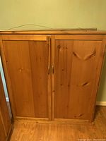 Closed solid wood cupboard showing two panel doors with metal handles and natural wood grain.