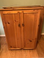 Front view of solid wood wooden shelf unit with closed double doors and metal ring handles.