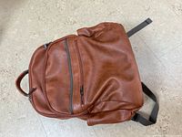 Brown leather Bugatti backpack laying flat showing front with multiple zippered compartments and side pockets.