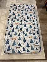 Photo of crib mattress showing full length with fitted sheet featuring illustrations of pine trees and woodland animals like foxes, wolves, and polar bears.