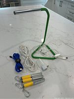 Green desk lamp, white extension cord, blue and white USB cables, 3 yellow and silver LED flashlights, white night light adapter placed on white countertop.